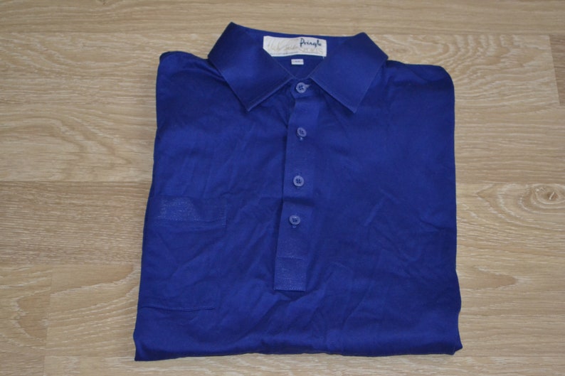 May include: A blue polo shirt with a white label that says "Pringle". The shirt has a button-up collar and a pocket on the left side.