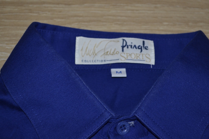 May include: A blue collared shirt with a white label that reads "Willie Faldo Collection Pringle Sports" and a size "M" label.