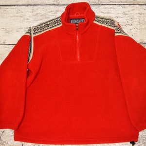 Puede incluir: Sudadera de forro polar roja con cierre de cremallera de media cremallera y un yugo estampado. El yugo presenta un diseño geométrico blanco, negro y azul.