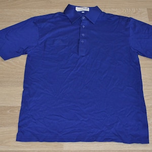 May include: A blue short-sleeved polo shirt with a pocket on the left chest and a small embroidered logo on the right sleeve.