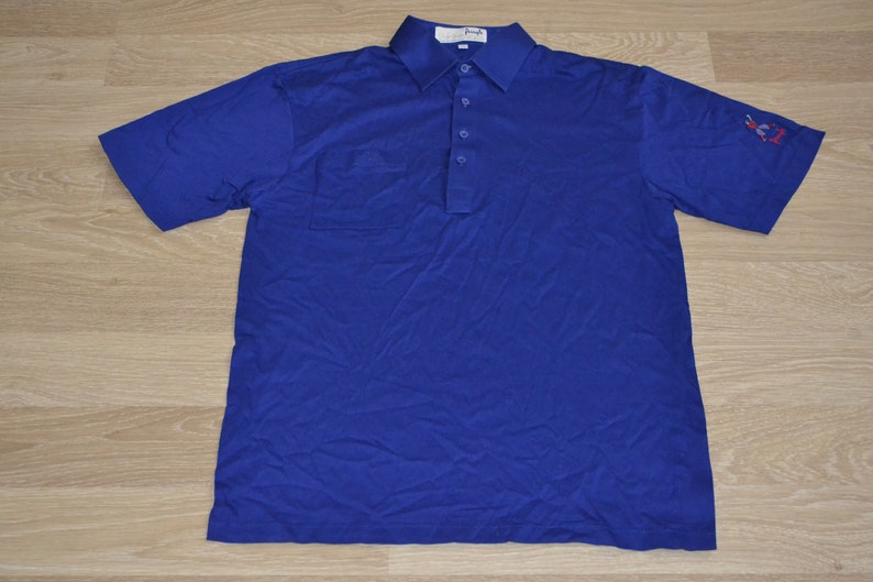 May include: A blue short-sleeved polo shirt with a pocket on the left chest and a small embroidered logo on the right sleeve.