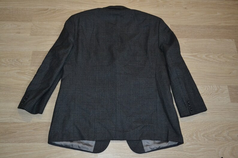 May include: A dark gray blazer with a subtle checkered pattern. The blazer has a single button closure and long sleeves.