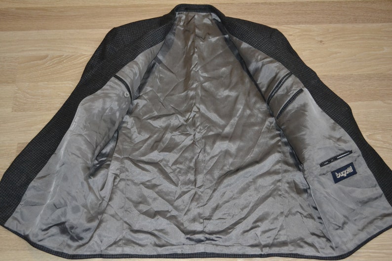 May include: A black and gray checkered blazer with a gray satin lining. The blazer has a pocket on the inside with a "Bugatchi" label.