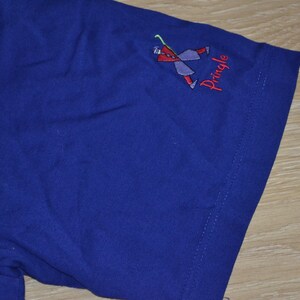 May include: A blue t-shirt with a small embroidered logo of a stick figure playing golf. The logo says "Pringle".