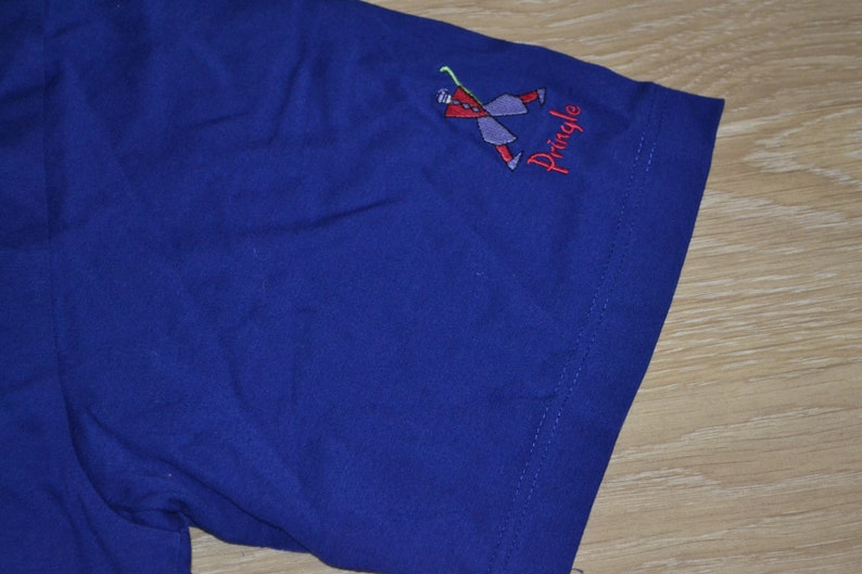 May include: A blue t-shirt with a small embroidered logo of a stick figure playing golf. The logo says "Pringle".
