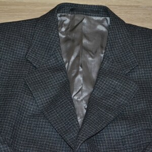 May include: A dark gray blazer with a subtle checkered pattern. The blazer has a satin lining and a classic notched lapel.