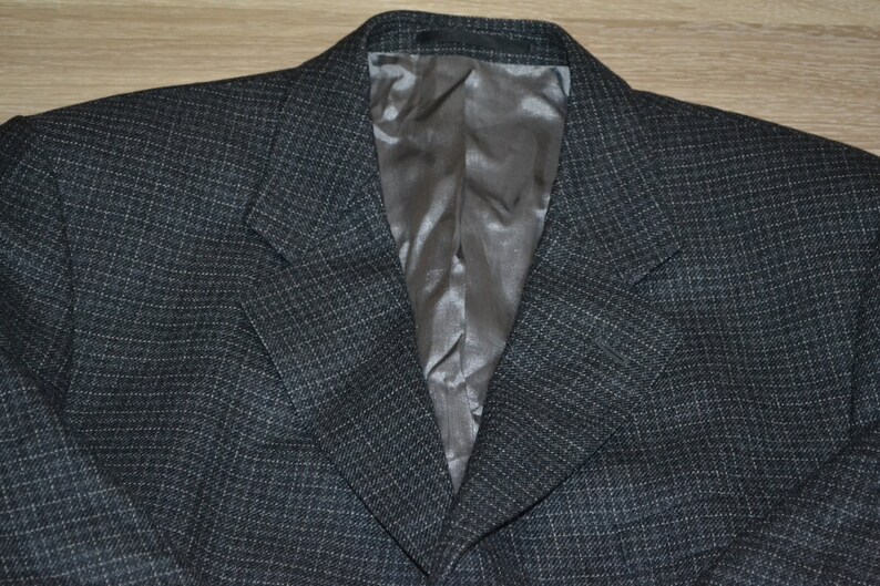 May include: A dark gray blazer with a subtle checkered pattern. The blazer has a satin lining and a classic notched lapel.