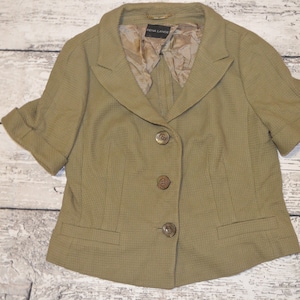 May include: A short-sleeved, olive green blazer with a notched collar and three buttons. The blazer has a textured fabric and a lined interior.