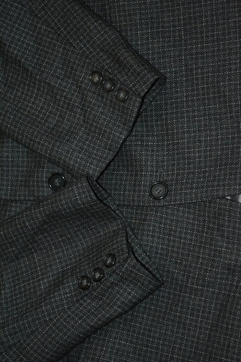 May include: A dark gray blazer with a subtle pinstripe pattern. The blazer has a double-breasted closure with four buttons on each side.