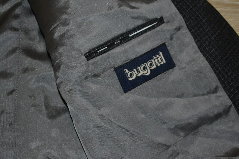 May include: A close-up of the inside of a gray jacket with a navy blue label that says "bugatti" in white lettering.