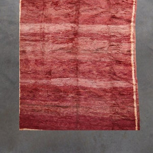 Puede incluir: Una alfombra de rayas rojas y blancas con un patrón sutil. La alfombra tiene un borde con flecos y está hecha de un material suave y tejido.