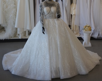 May include: A white wedding dress with a high neckline and long sleeves. The dress has a fitted bodice and a full skirt with a sparkly, glittery fabric.
