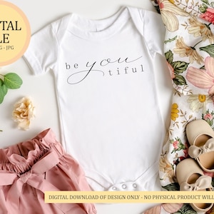 Könnte beinhalten: Ein weißer Baby-Strampler mit dem Text "be you tiful" in schwarzer Schrift. Der Strampler liegt auf einer weißen Oberfläche mit einem floralen Stoff und einem Paar beigen Babyschuhen.
