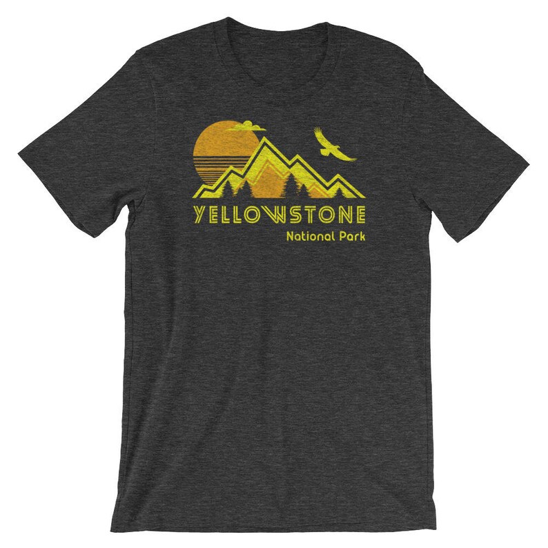 May include: A dark grey t-shirt with a yellow graphic of mountains, a sun, and a bird. The text "Yellowstone National Park" is printed in yellow below the graphic.