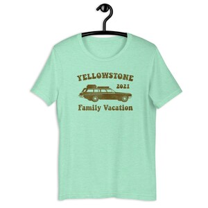 May include: A light green t-shirt with a brown graphic of a vintage station wagon with luggage on the roof. The text "Yellowstone 2021 Family Vacation" is printed below the car.