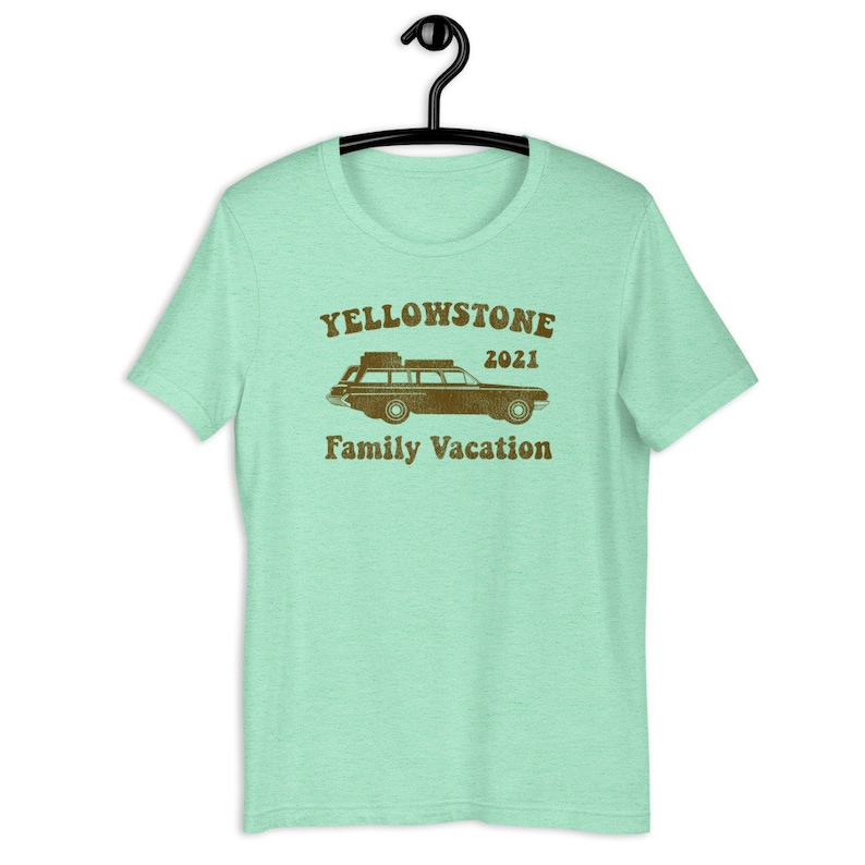 May include: A light green t-shirt with a brown graphic of a vintage station wagon with luggage on the roof. The text "Yellowstone 2021 Family Vacation" is printed below the car.