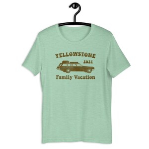 May include: A light green t-shirt with a brown graphic of a vintage station wagon with luggage on the roof. The graphic also includes the text "Yellowstone 2021 Family Vacation".
