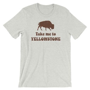 May include: A light grey t-shirt with a brown silhouette of a bison and the text "Take me to Yellowstone" printed on the front.