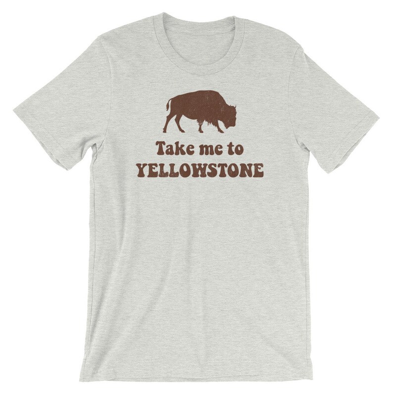May include: A light grey t-shirt with a brown silhouette of a bison and the text "Take me to Yellowstone" printed on the front.