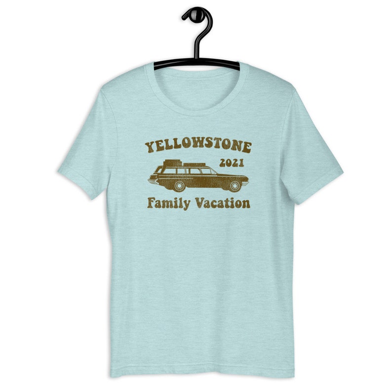 May include: A light blue t-shirt with a brown vintage-style graphic of a station wagon with luggage on the roof. The graphic says "Yellowstone 2021 Family Vacation".