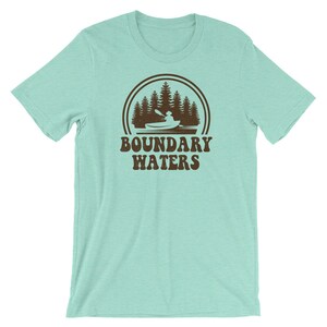 May include: A light blue t-shirt with a brown graphic of a canoe in a lake with trees and the text "Boundary Waters".