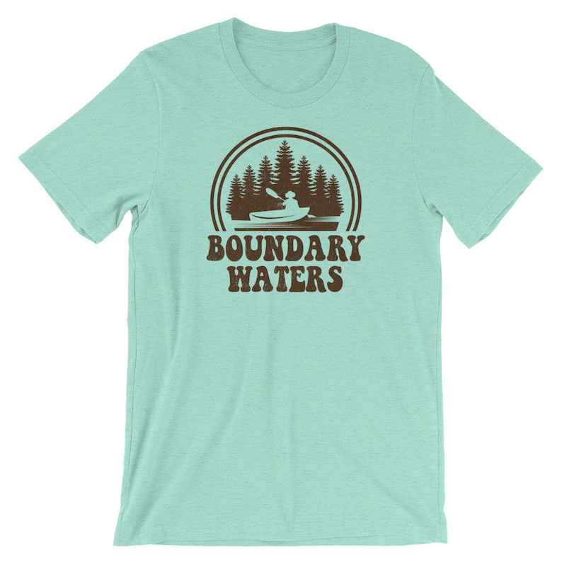 May include: A light blue t-shirt with a brown graphic of a canoe in a lake with trees and the text "Boundary Waters".