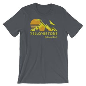May include: A dark gray t-shirt with a yellow graphic of mountains, a sun, and a bird. The text "Yellowstone National Park" is printed in yellow below the graphic.