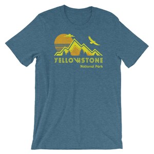 May include: A blue t-shirt with a yellow and orange graphic of mountains, a sun, and a bird. The text "Yellowstone National Park" is printed in yellow below the graphic.