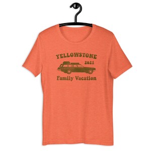 May include: Orange t-shirt with a vintage-style graphic of a station wagon with luggage on the roof. The text "Yellowstone 2021 Family Vacation" is printed on the shirt.