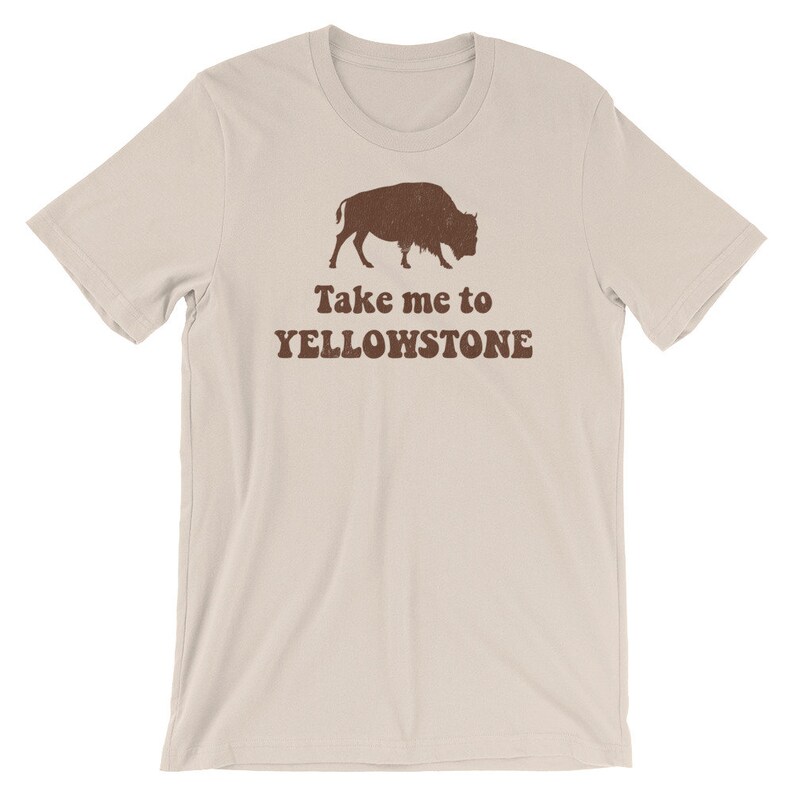 May include: A beige t-shirt with a brown silhouette of a bison and the text "Take me to Yellowstone" printed on the front.