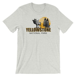May include: A heather grey t-shirt with a black and white illustration of an elk standing in front of a yellow sun and two pine trees. The text "Yellowstone National Park" is printed in black on the shirt.