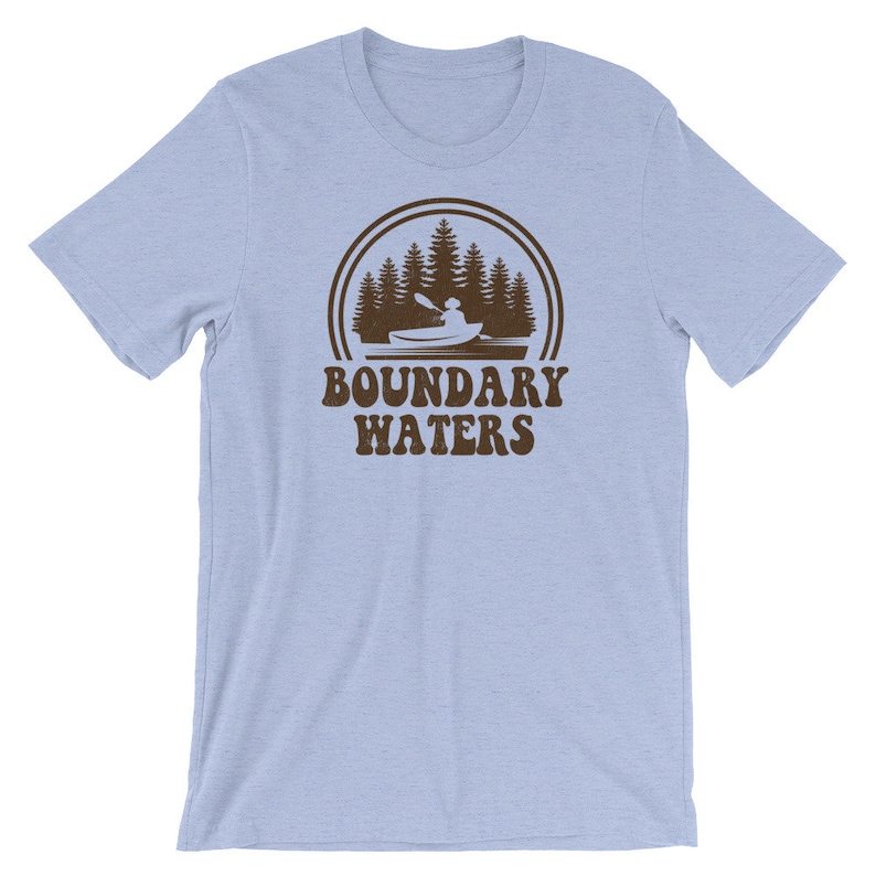 May include: Light blue t-shirt with a brown graphic of a person kayaking in a lake with trees in the background. The text "Boundary Waters" is below the graphic.