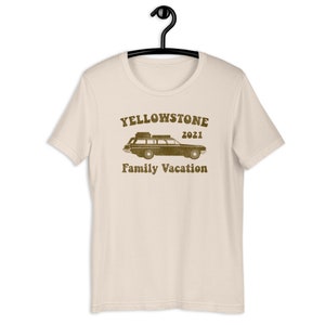 May include: A beige t-shirt with a brown graphic of a vintage station wagon with luggage on the roof. The text "Yellowstone 2021 Family Vacation" is printed below the car.