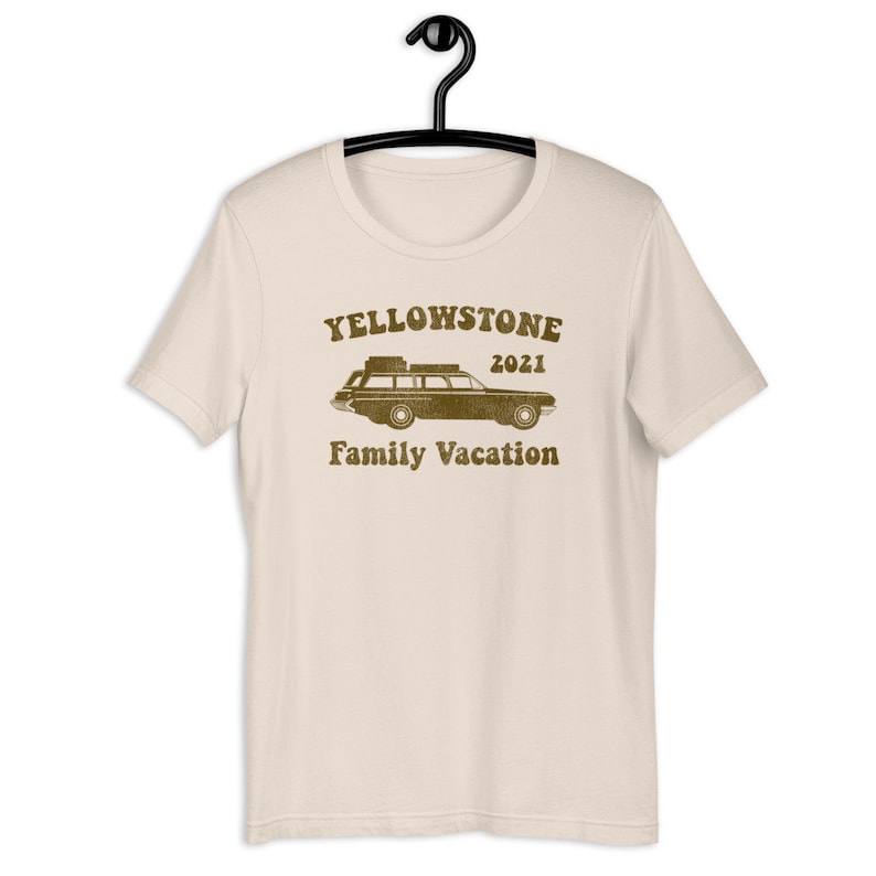 May include: A beige t-shirt with a brown graphic of a vintage station wagon with luggage on the roof. The text "Yellowstone 2021 Family Vacation" is printed below the car.