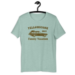 May include: A light blue t-shirt with a brown vintage-style graphic of a station wagon with luggage on the roof. The text "Yellowstone 2021 Family Vacation" is printed below the car.