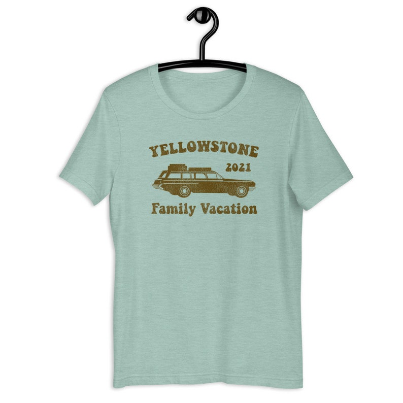 May include: A light blue t-shirt with a brown vintage-style graphic of a station wagon with luggage on the roof. The text "Yellowstone 2021 Family Vacation" is printed below the car.