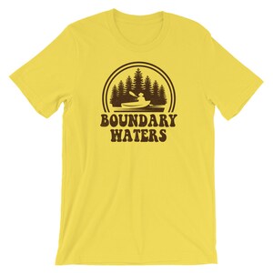 May include: Yellow short-sleeved t-shirt with a brown graphic of a person kayaking in a lake with trees in the background. The text "BOUNDARY WATERS" is below the graphic.
