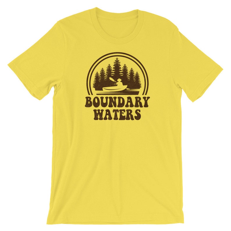 May include: Yellow short-sleeved t-shirt with a brown graphic of a person kayaking in a lake with trees in the background. The text "BOUNDARY WATERS" is below the graphic.