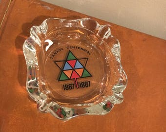 May include: A clear glass ashtray with a colorful logo that says "Canada Centennial 1867-1967".