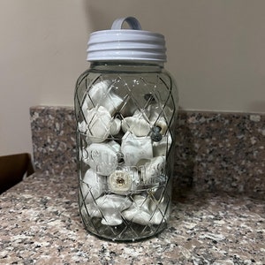 May include: A clear glass jar with a white lid and handle, filled with white ceramic drawer knobs. The jar has a diamond pattern and the text "Better Homes & Gardens" printed on the side.
