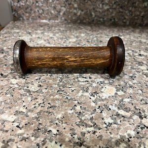 Könnte beinhalten: Eine Holzspule mit einem Metallring an einem Ende. Die Spule ist braun und hat eine glatte Oberfläche.