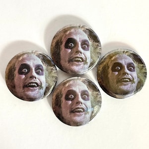 May include: Four round button badges featuring a close-up image of a character with green hair and black makeup. The character is looking directly at the viewer with a wide-eyed, surprised expression.
