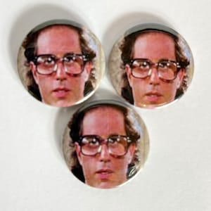 May include: Three round button badges featuring a man with brown hair wearing glasses. The man is wearing a white shirt and has a serious expression.