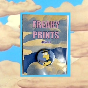 Peut inclure: Un personnage de dessin animé jaune avec des cheveux bleus et un pistolet est sur un bouton bleu et blanc. Le bouton est sur une carte avec le texte "FREAKY PRINTS .COM.AU" en lettres roses et noires.