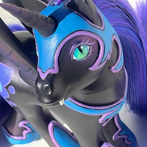 Puede incluir: Una figura de unicornio negro con crin y cola de color azul oscuro y morado. La figura presenta un cuerno negro, ojos verdes y detalles de armadura azul y morada en la cabeza y el cuerpo. Se ve un pequeño colmillo blanco.