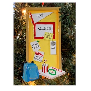 May include: A yellow door-shaped Christmas ornament with the name "Allison" and the text "CSU" on it. The door has a red frame and a blue backpack, a pizza box, and a red and white cup with a straw on the bottom. There are several sticky notes on the door with the text "Exam Today!" "Party This Saturday" and "In Class-Txt.Me!"