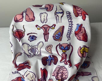 May include: White surgical scrub cap with a repeating pattern of human anatomy illustrations in red, pink, and blue. The design includes organs, bones, and other anatomical details. The cap has a tie closure.