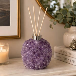 May include: A spherical reed diffuser bottle covered in textured purple amethyst crystals. The bottle features a silver-toned metal collar at the neck and contains four light-colored wooden diffuser reeds extending upward from the opening.