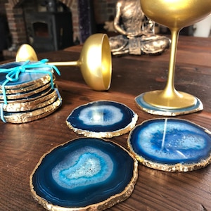 Peut inclure: Ensemble de quatre sous-verres en agate bleue avec bordure dorée. Les sous-verres sont ronds et ont un aspect naturel et organique. Ils sont parfaits pour protéger vos meubles des rayures et des déversements.