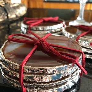 May include: Set of four agate coasters with silver-plated edges. The coasters are tied together with a red ribbon.
